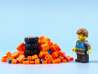 pile of orange pieces and 4 wheels stacked, confused minifigure at the right