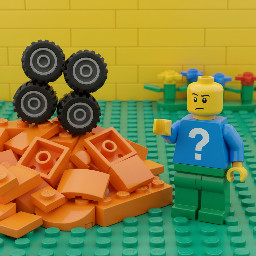 pile of orange pieces and 4 wheels stacked at the left, confused minifigure at the right