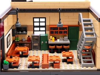 🧱 Concept général  Il s'agit d'un diorama LEGO représentant exclusivement l'intérieur d'un café, ouvert sur l'avant pour que l'on puisse voir l'ensemble de l'aménagement en regardant le modèle de face.  Le café possède :  un rez-de-chaussée ; un premier étage ; un seul escalier métallique ; une ambiance chaleureuse, de type café/restaurant.  Il ne doit y avoir :  aucun extérieur ; aucun personnage ; aucune référence ou easter egg de pop culture. 🏠 REZ-DE-CHAUSSÉE 🍳 La cuisine — partie gauche  La cuisine occupe toute la partie gauche du diorama.  ⚠️ Point important : elle s'étend depuis le mur du fond jusqu'au côté ouvert du diorama.  Elle n'est donc pas uniquement située au fond. 🚪 Le mur entre la cuisine et le bar  La cuisine et le bar sont séparés par un véritable mur.  Ce mur sépare clairement les deux espaces. Il part du fond et sépare la cuisine du bar. Une porte est intégrée dans ce mur, vers le fond du diorama. Cette porte permet au personnel de passer du bar à la cuisine.  Il ne doit donc pas y avoir de grande ouverture entre la cuisine et le bar.  🍹 Le bar  Le bar se situe à droite de la cuisine.  Il doit :  être large et imposant ; être clairement séparé de la cuisine par le mur ; être orienté de manière à s'étendre de l'avant vers le fond du diorama ; disposer de bouteilles et de verres sur des étagères situées derrière le comptoir.  ⚠️ Il ne doit y avoir aucune table devant le bar ni à sa gauche.  Toutes les tables du rez-de-chaussée sont situées à droite du bar.  🪑 Les tables du rez-de-chaussée  Il y a exactement deux rangées de tables avec banquettes.  Rangée 1 : au fond La première rangée est située dans la partie arrière de l'espace de restauration. Les banquettes de cette rangée doivent être directement contre le mur du fond du diorama.  Les tables ne doivent donc pas flotter au milieu de la pièce : les banquettes arrière touchent ou longent clairement le mur du fond.  Rangée 2 : plus vers l'avant Une deuxième rangée se trouve devant la première. Elle est également composée de tables avec banquettes.  Toutes ces tables se trouvent à droite du bar.  🚻 Toilettes  La porte des toilettes :  est verte ; se trouve au rez-de-chaussée ; est placée au fond du diorama.  Elle doit être distincte de la porte permettant d'accéder à la cuisine.  🚪 Entrée du café  La porte d'entrée est située :  dans le mur latéral droit ; au rez-de-chaussée.  Elle ne doit absolument pas être placée :  sur la façade ouverte ; dans un mur face à nous.  Elle doit être intégrée au mur droit, celui qui s'étend de l'avant vers le fond du diorama.  🪜 L'escalier  Il y a un seul escalier :  métallique ; de style industriel ; situé au fond à droite ; permettant d'accéder au premier étage. 🏢 PREMIER ÉTAGE  Le premier étage doit être suffisamment grand et clairement visible.  Il comprend exactement deux rangées de tables avec banquettes.  Rangée du fond  ⚠️ Même règle qu'au rez-de-chaussée : la rangée de tables située au fond doit avoir ses banquettes directement contre le mur du fond du diorama.  Deuxième rangée Elle se trouve devant la rangée du fond. Elle laisse un espace de circulation entre les différentes zones.  Le premier étage possède également :  un garde-corps métallique donnant sur le rez-de-chaussée ; l'arrivée de l'unique escalier.