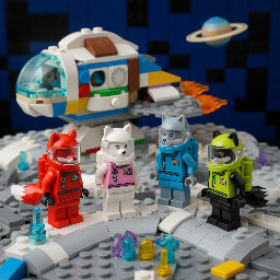 The four astronauts: the fox with the red spacesuit and the red space helmet where you can see his tail, the white fox with the pink spacesuit and the pink space helmet where you can see his tail, the wolf with the blue spacesuit and the blue space helmet where you can see his tail and the black wolf with the green spacesuit and the green space helmet where you can see his tail